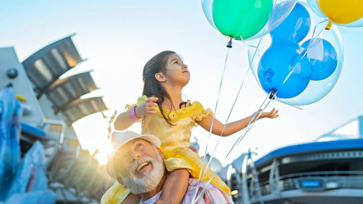 little girl sitting on grandpa's shoulder with balloons in her hand at Walt Disney World in Orlando, Florida, USA